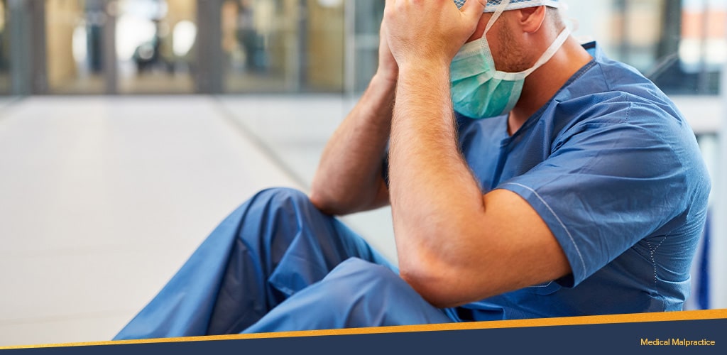 medical malpractice, a man in scrubs with his head in his hands